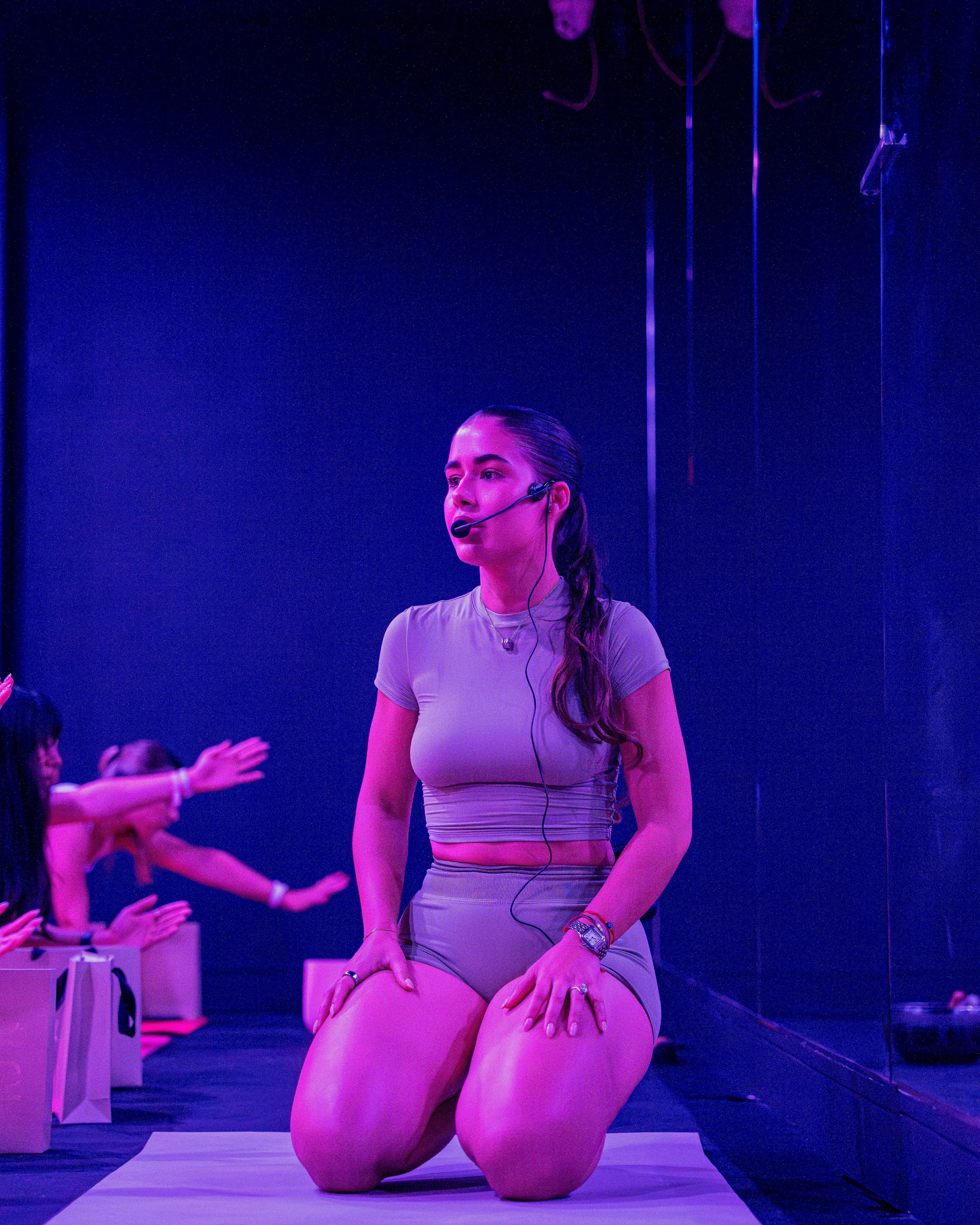 Laura Lezcano coaching a Pilates class under violet studio lighting